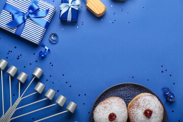 Frame made of plate with donuts, menorah and gifts for Hanukkah celebration on blue background