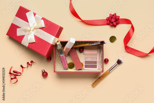 Gift box with makeup products and Christmas decor on beige background