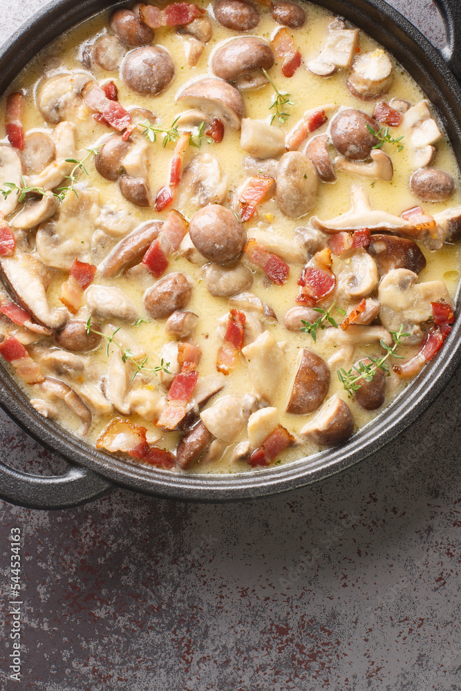 Delicious Champignon mushrooms in a spicy creamy wine sauce with bacon, garlic and parmesan cheese close-up in a frying pan on the table. Vertical top view from above Delicious Champignon mushrooms in a spicy creamy wine sauce with bacon, garlic and parmesan cheese close-up in a frying pan on the table. Vertical top view from above