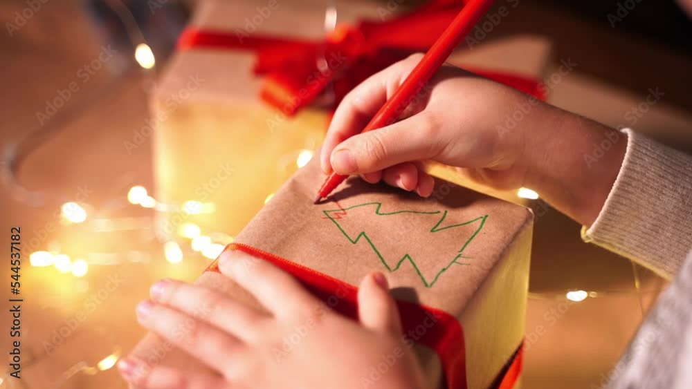 Family packing Christmas gifts in evening. Child and Grandfather hand wrapping the present box with craft paper and red ribbon. Happy time together.