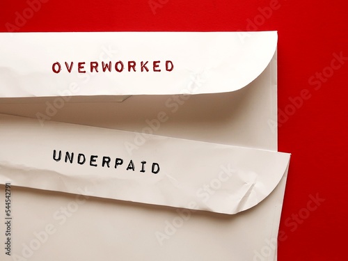 Office envelopes with handwritten text OVERWORKED and UNDERPAID, means employees or workers who work too hard or too long but get paid less than what they deserve photo