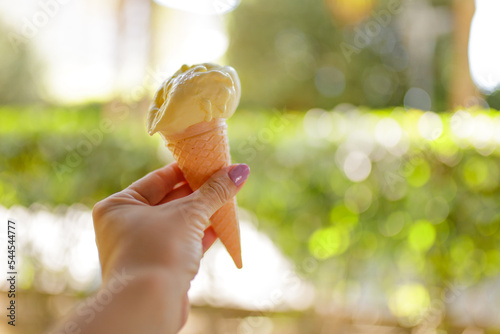 Hand holding a crispy cone with ice cream against blurry summer garden