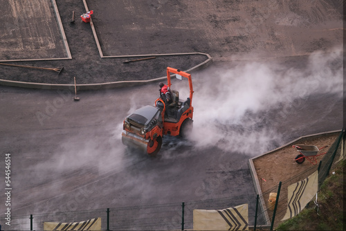 Orange asphalt paver machine laying asphalt road in the rainy day and steam rising from the asphalt, top view	
