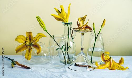 flowers in glass vases. levitation from flowers and glass goblets. still life with flowers and splashes. yellow lilies in a glass. still life of flowers and glasses on a white textured tablecloth