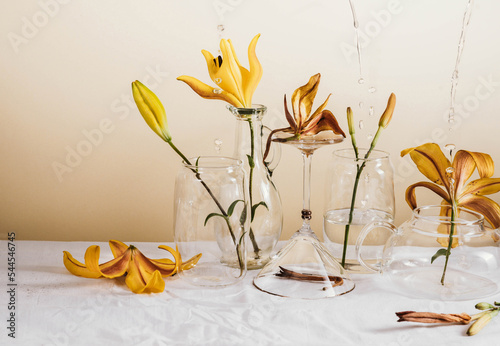 flowers in glass vases. levitation from flowers and glass goblets. still life with flowers and splashes. yellow lilies in a glass. still life of flowers and glasses on a white textured tablecloth