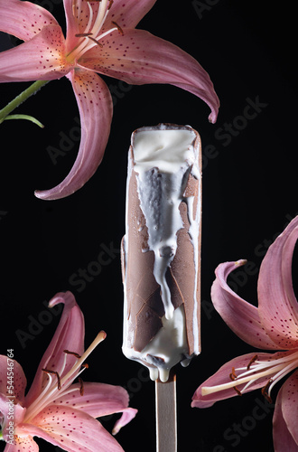 melting ice cream on a stick. ice cream covered with chocolate icing on a wooden stick. ice cream and pink lilies. ice cream and flowers. milk ice cream drops