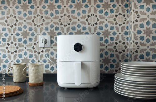 Air fryer machine, mugs, and dishes in modern domestic kitchen. Technology home smart device