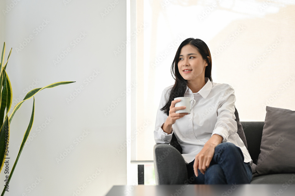 Young Asian woman relaxes sipping morning coffee while chilling in her living room. Young Asian woman relaxes sipping morning coffee while chilling in her living room.
