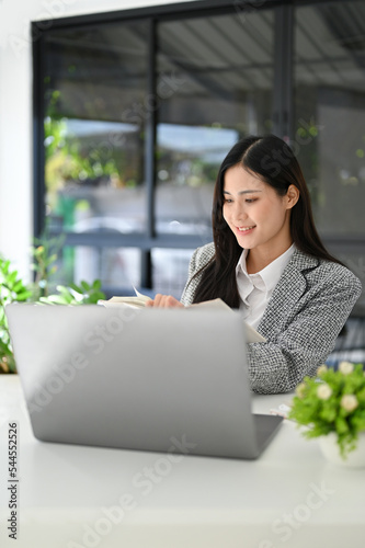 Attractive Asian businesswoman reading something on her notebook while working in her office.