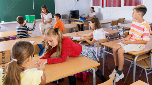 Girl and boy are sitting at the desk and talking about life in the classroom