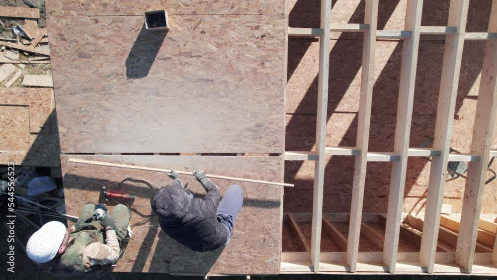 Carpenters hammering nail into OSB panel on the roof top of future