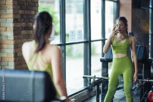 Asian woman beaultiful building slim body in green sportswear with smartphone taking mirror selfie in gym. Healthcare and healthy lifestyle concept.