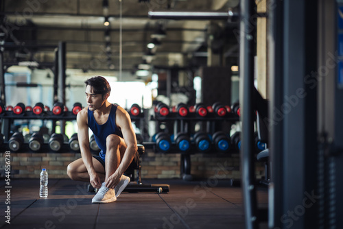 Asian man healthy preparing before workout training. Active Asian man tying shoelaces on sports shoes. Young male athlete legs in sneakers and hands tying shoelaces in fitness gym.
