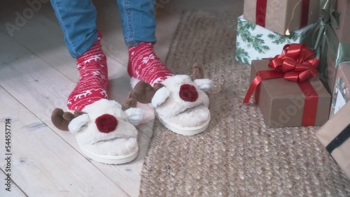 Merry Christmas. A teenage child wears slippers for the new year. Slippers in the form of Christmas deer. Female Feet in red Christmas socks wear slippers