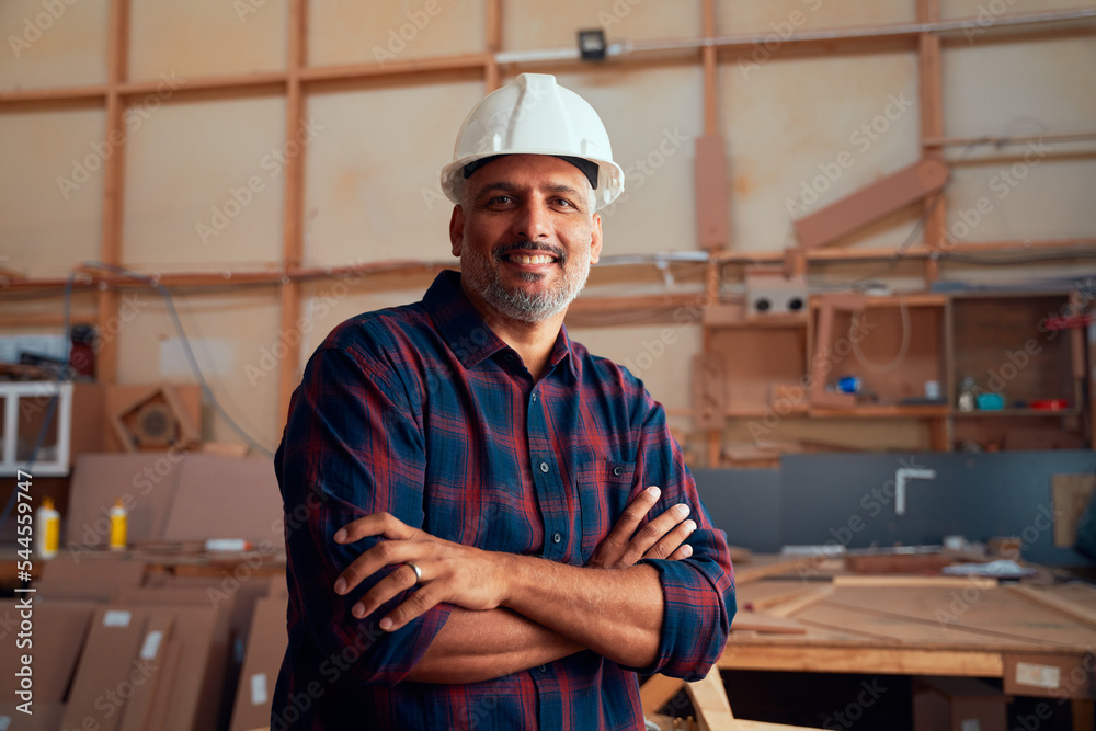 Portrait of happy mid adult man in safety helmet with arms crossed in woodworking factory Portrait of happy mid adult man in safety helmet with arms crossed in woodworking factory