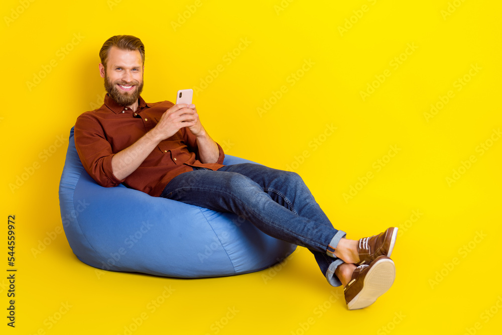 Full size photo of positive young man sit comfy bag hold use telephone