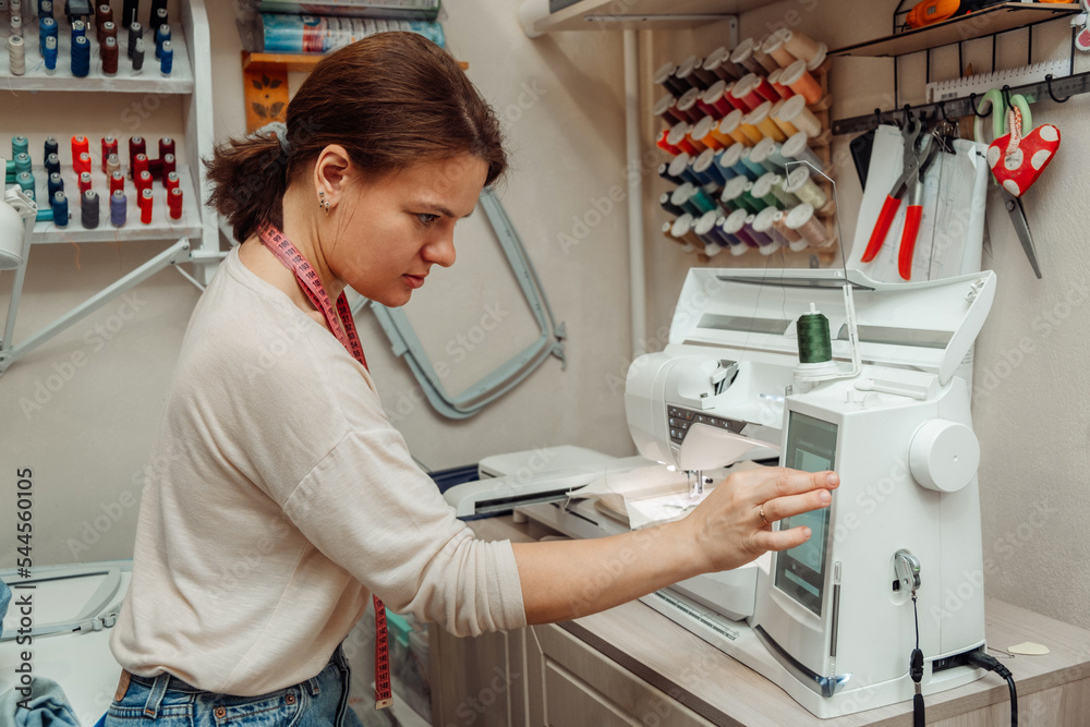 A woman tailor makes embroidery on an embroidery machine in a home workshop.Mending clothes concept,small business.