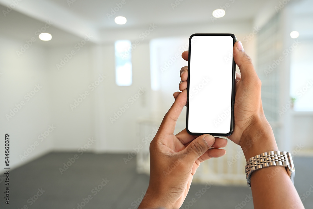 Woman hands holding smart phone over blurred bright living room background. Empty screen for your advertise design Woman hands holding smart phone over blurred bright living room background. Empty screen for your advertise design