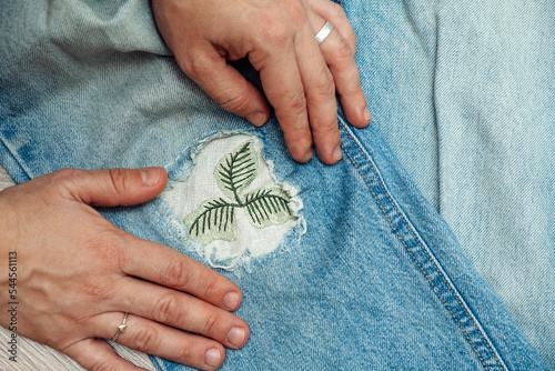 A woman mends jeans, sews a patch on a hole, hands close-up.Mending clothes concept,reusing old jeans.