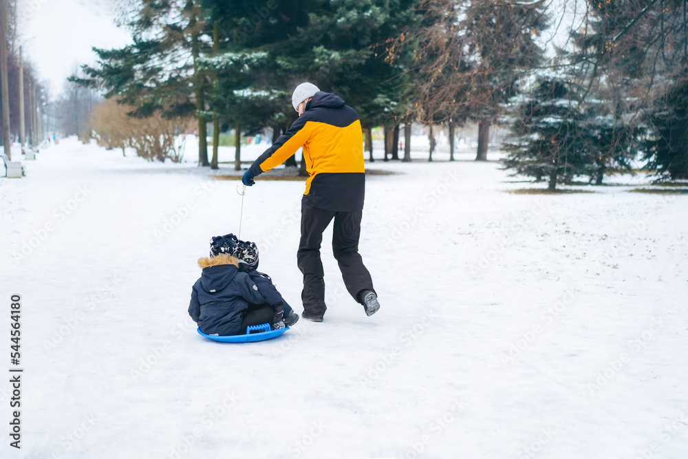 Dad ride his kids on sled in park. Winter activities. Happy family weekend on snowy day.