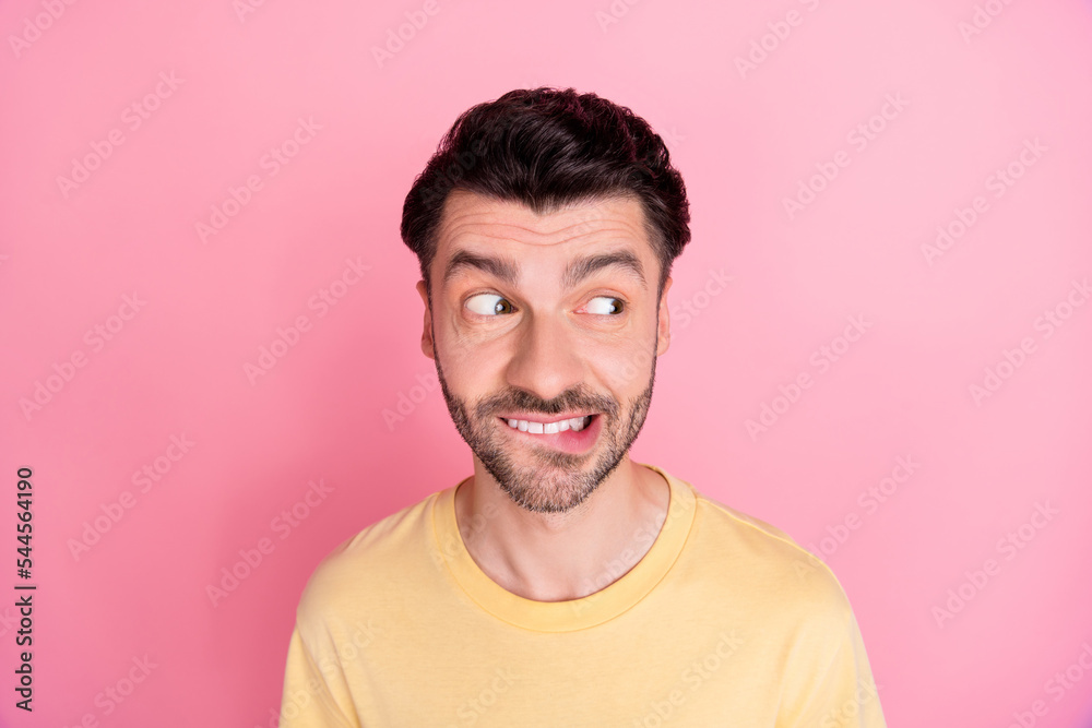 Photo of optimistic positive guy with brunet hairstyle yellow t-shirt bite lips look empty space isolated on pink color background Photo of optimistic positive guy with brunet hairstyle yellow t-shirt bite lips look empty space isolated on pink color background