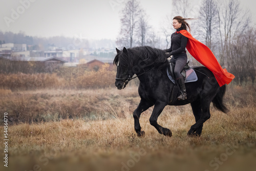 Beautiful girl in red cloak on black stallion
