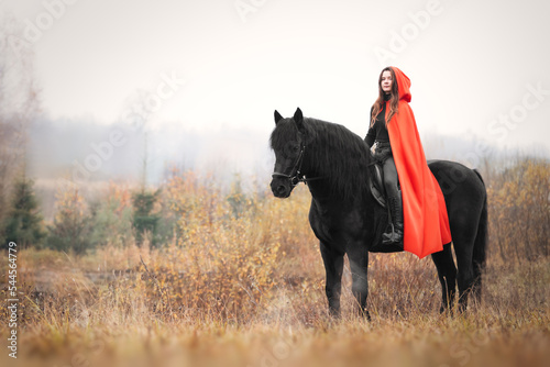 Beautiful girl in red cloak on black stallion