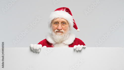 Happy Santa Claus looking out from behind blank sign isolated on white background with copy space
