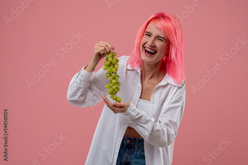 Laughing pink-haired girl holding a grapevine in her hands