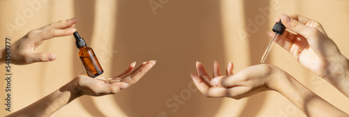Leinwand Poster Two pairs of female hands hold bottle of amber glass with cosmetic serum and pipette with moisturizing oil on light brown background, in rays of sunlight