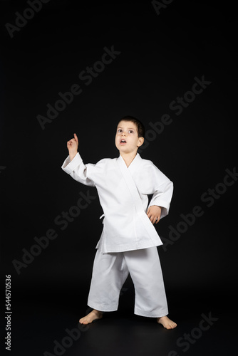 5 year old boy in kimono points his finger up at the black background, a place for text