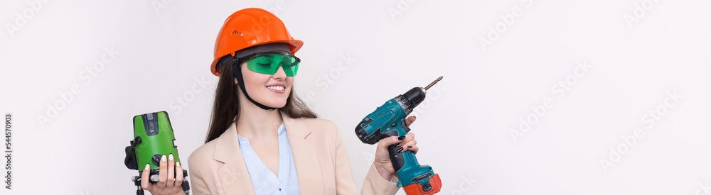 A girl in an orange helmet and a laser level in her hands on a white background. A girl in an orange helmet and a laser level in her hands on a white background.