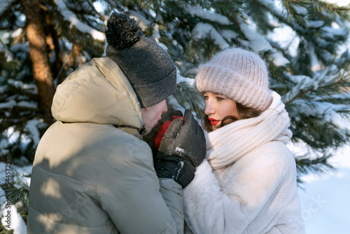 Guy warms the hand of his beloved with his breath. Loving couple in winter forest. Loving couple