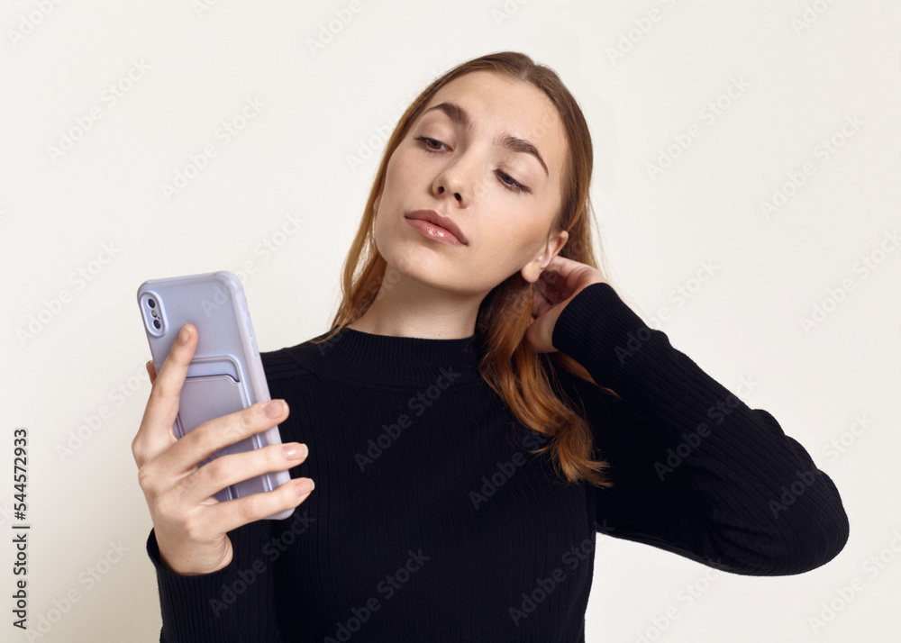 a cute woman in a black turtleneck stands on a white background and reads a message on her smartphone a cute woman in a black turtleneck stands on a white background and reads a message on her smartphone