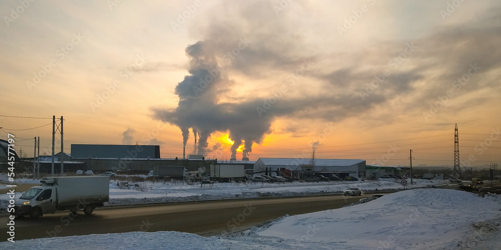 Traffic of cars on a suburban highway against the background of smoke from a thermal power plant and against the background of the evening sky at sunset