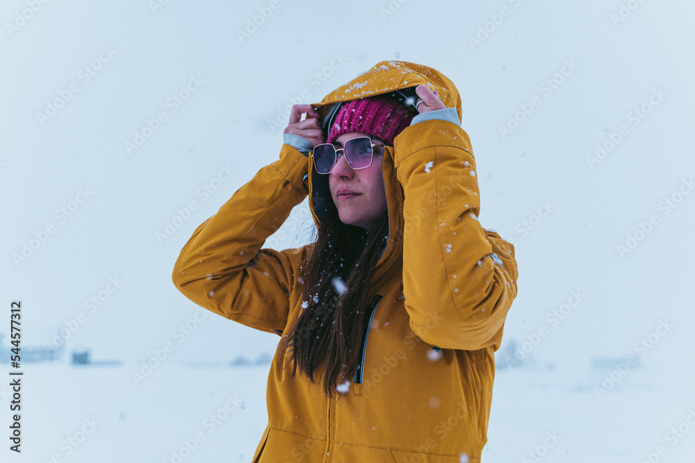 woman in the snow with yellow coat, hat and sunglasses