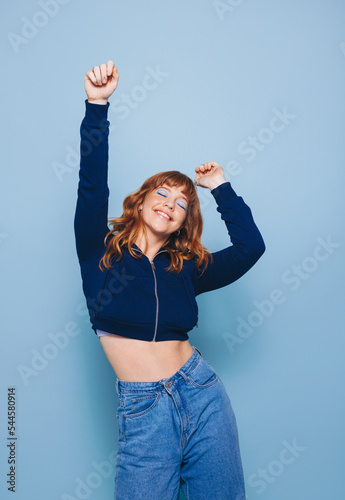 Happy young woman dancing and having fun while wearing a crop top and jeans in a studio photo