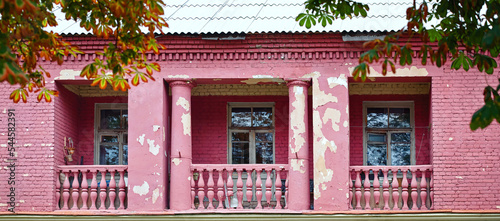 Old balcony with column and balustrade. Old balcony on purple building facade with cracked stucco wall