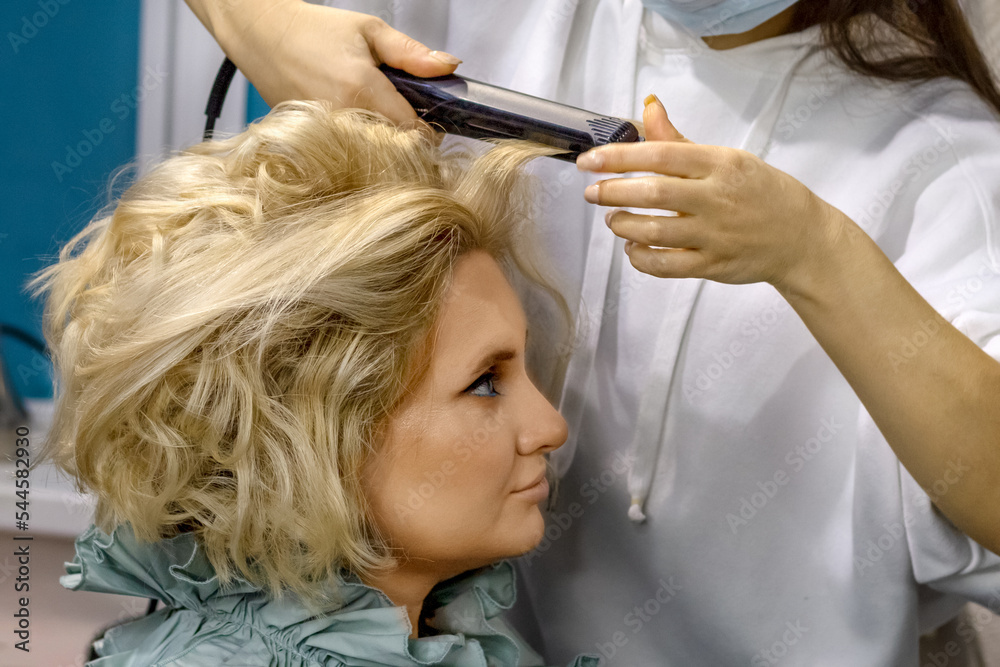 Fototapeta premium The hairdresser does the styling of the girl before the holiday party in the beauty salon. Creating a hairstyle.
