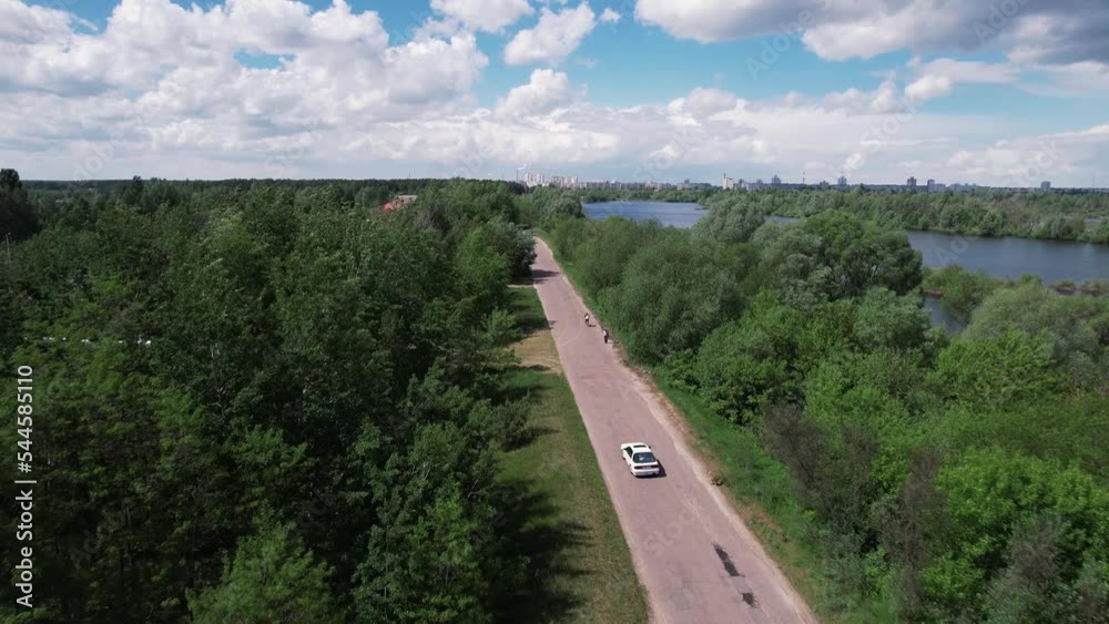 Top view of the road among the trees with the car and the panorama of the countryside with lakes and villages Top view of the road among the trees with the car and the panorama of the countryside with lakes and villages