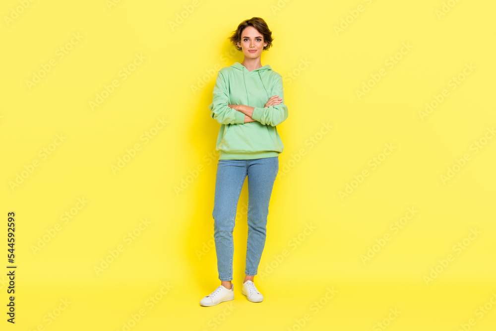 Full length photo of charming confident girl dressed green sweatshirt arms crossed smiling isolated yellow color background Full length photo of charming confident girl dressed green sweatshirt arms crossed smiling isolated yellow color background