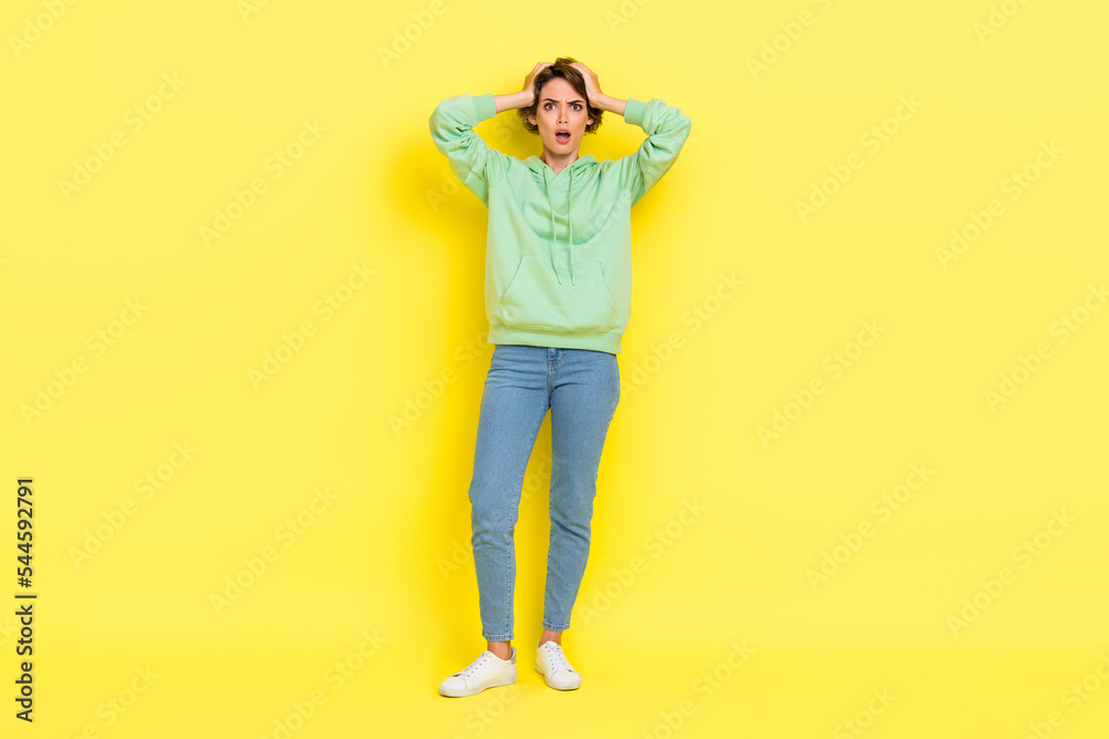 Full length photo of impressed shocked girl dressed green sweatshirt open mouth arms head isolated yellow color background Full length photo of impressed shocked girl dressed green sweatshirt open mouth arms head isolated yellow color background
