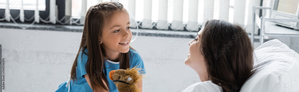 Smiling kid in patient gown looking at mom with toy in hospital ward, banner. Smiling kid in patient gown looking at mom with toy in hospital ward, banner.