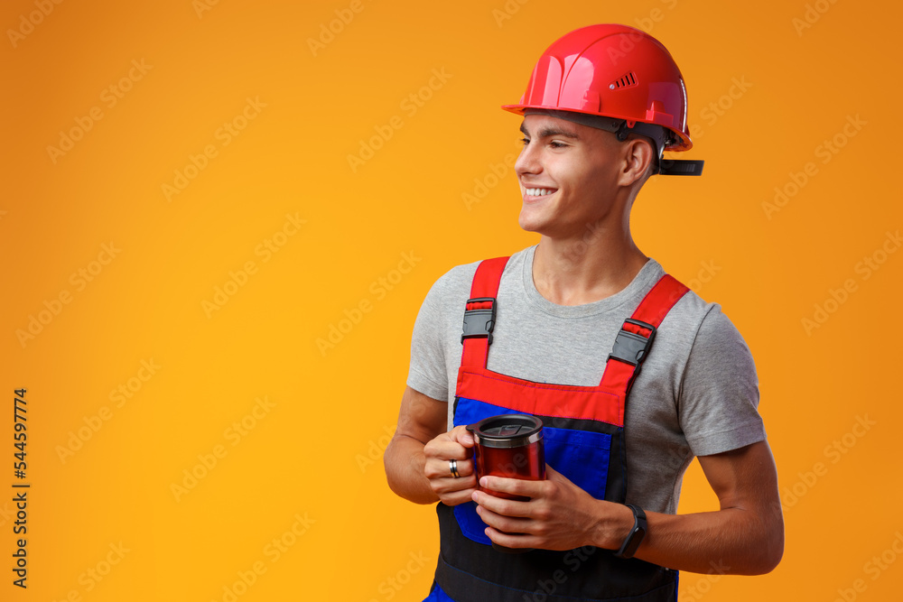 Young builder in uniform holding coffee cup on yellow background Young builder in uniform holding coffee cup on yellow background