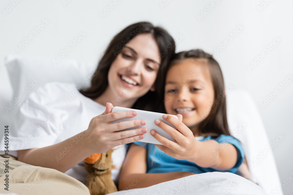 Positive woman and child using smartphone on bed in hospital. Positive woman and child using smartphone on bed in hospital.