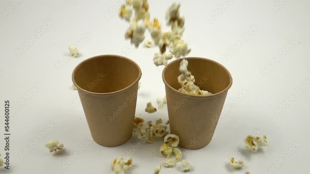 A lot of white salty popcorns fall into two paper cups, background, slow motion A lot of white salty popcorns fall into two paper cups, background, slow motion