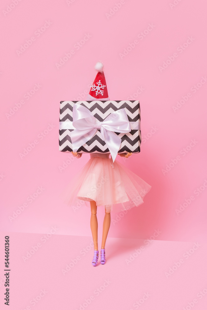 Christmas shopping minimal concept. A doll with Xmas present in her hands on pink background