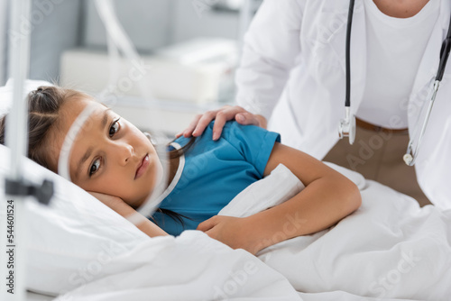 Pediatrician calming upset girl on hospital bed.