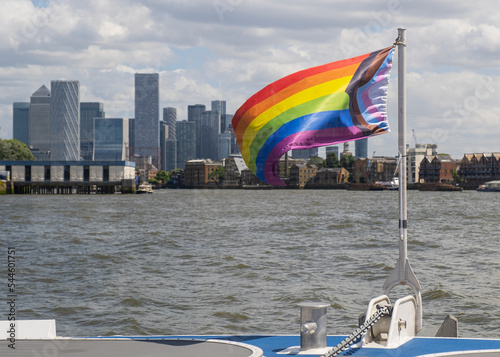 Pride flag in front of Canary Wharf skyscrapers. View from the river Thames.