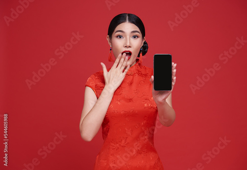 Happy Asian woman wearing traditional cheongsam qipao dress showing mobile phone isolated on red background. photo